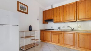 A kitchen with wooden cabinets, a white refrigerator, a tiled backsplash, and a shelf unit. - Three-Room Apartment with Garden 100 Meters from the Beach - Sole e Mare Tourist Village (Rio)