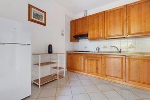 Eine Küche mit Holzschränken, einem weißen Kühlschrank, einer gefliesten Spritzschutzwand und einem Regalsystem.