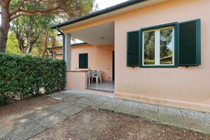 A building with a covered patio, a table with chairs, and a door leading to an interior space. - Three-Room Apartment with Garden 100 Meters from the Beach - Sole e Mare Tourist Village (Rio)