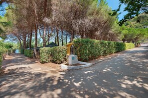 A paved pathway lined with trees and a small structure with a directional sign. - Three-Room Apartment with Garden 100 Meters from the Beach - Sole e Mare Tourist Village (Rio)