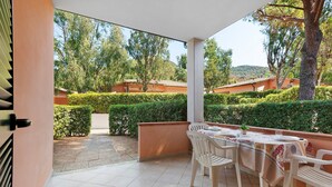 Un patio cubierto con una mesa lista para comer, rodeado de vegetación y edificios al fondo.
