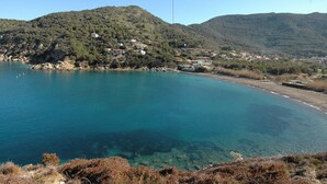 A coastal landscape with clear blue waters, a hillside with scattered buildings, and a visible road leading to the beach. - Three-Room Apartment with Garden 100 Meters from the Beach - Sole e Mare Tourist Village (Rio)