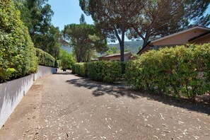 A paved driveway leading to a building with a white exterior and a red roof, surrounded by dense greenery and trees. - Three-Room Apartment with Garden 100 Meters from the Beach - Sole e Mare Tourist Village (Rio)