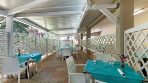 An outdoor patio area with tables and chairs, covered by a white roof, and surrounded by white lattice fencing. - Three-Room Apartment with Garden 100 Meters from the Beach - Sole e Mare Tourist Village (Rio)