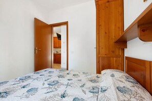 A bedroom with a bed, wooden wardrobe, and a kitchen visible through an open door. - Three-Room Apartment with Garden 100 Meters from the Beach - Sole e Mare Tourist Village (Rio)