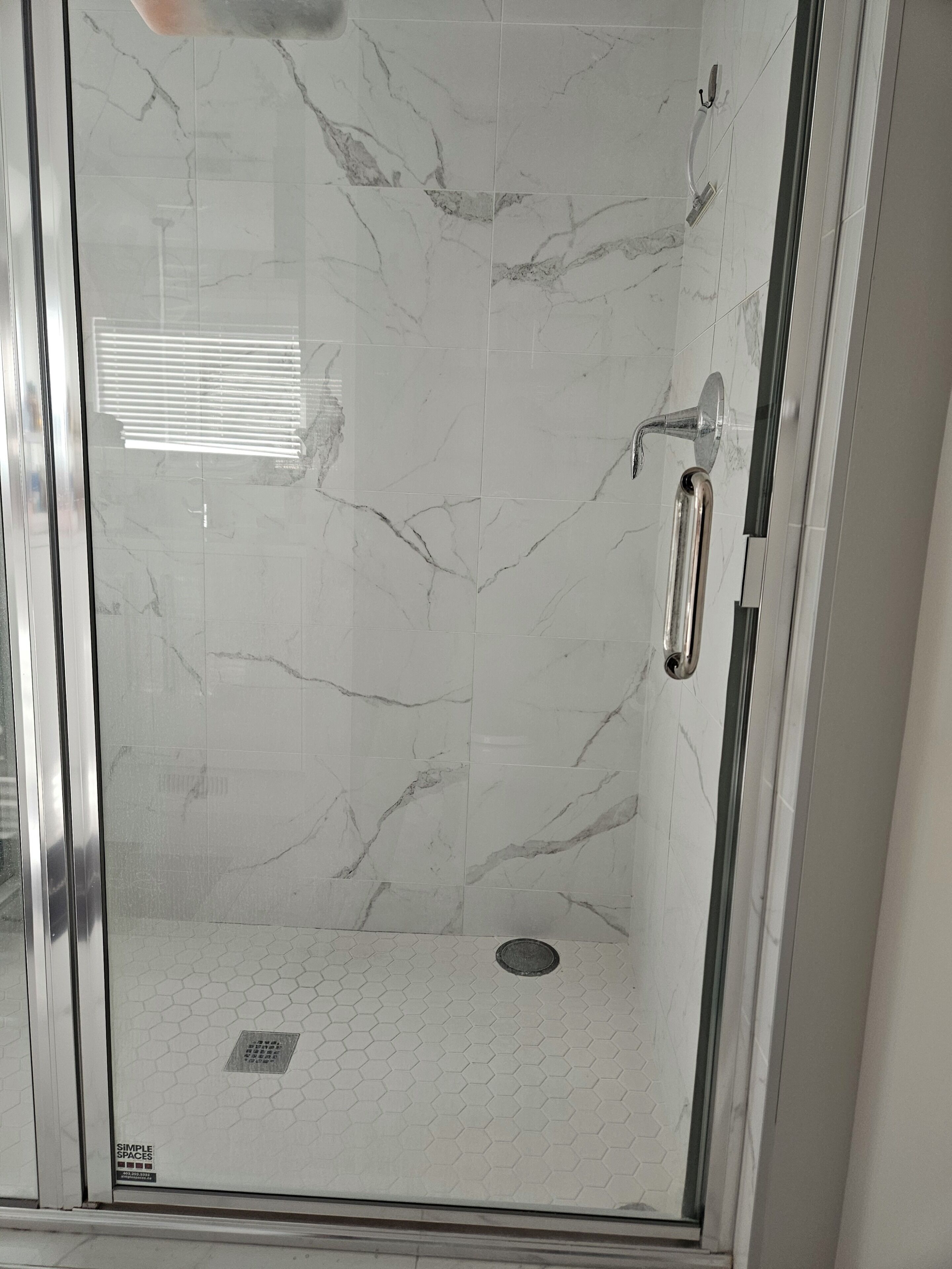 Une douche fermée par des parois de verre, avec un sol en marbre et une barre d’appui.