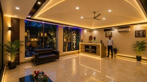 A hotel lobby with a reception desk, a sofa, a coffee table with flowers, and a large window overlooking a street. - HOTEL RONIT ROYAL - DELHI AIRPORT  (New Delhi)