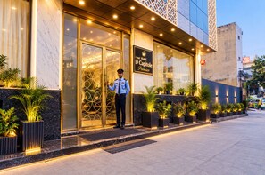 Entrada de un hotel con un guardia de seguridad, un cartel que dice 'Hotel D Capitole Premier' y plantas en macetas a lo largo del pasillo.