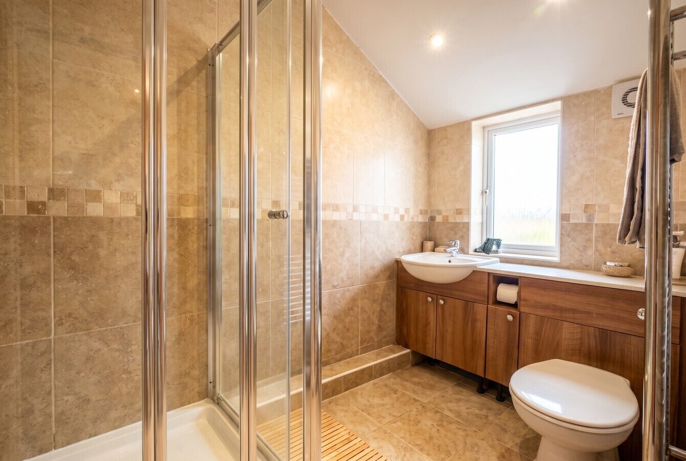 Een badkamer met een douchecabine van glas, een wastafel en een toilet.