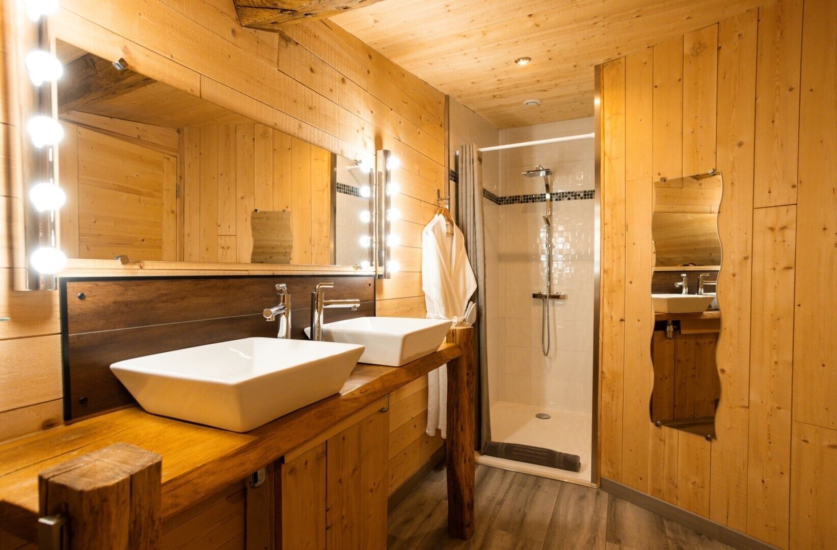 Une salle de bain en bois avec deux lavabos, un miroir avec éclairage intégré et un espace douche.
