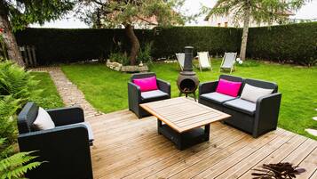 Une terrasse aménagée avec du mobilier d’extérieur, une table centrale et un élément décoratif en forme de foyer.
