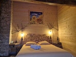 Una habitación de madera con una cama, dos lámparas de pared, un cuadro y una pequeña mesa de madera.