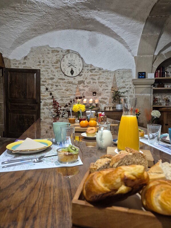 Un comedor rústico con paredes de piedra, una mesa de madera dispuesta con artículos para el desayuno y un reloj en la pared.