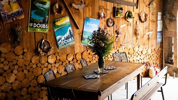A rustic wooden interior with a long dining table, benches, and a stone wall.