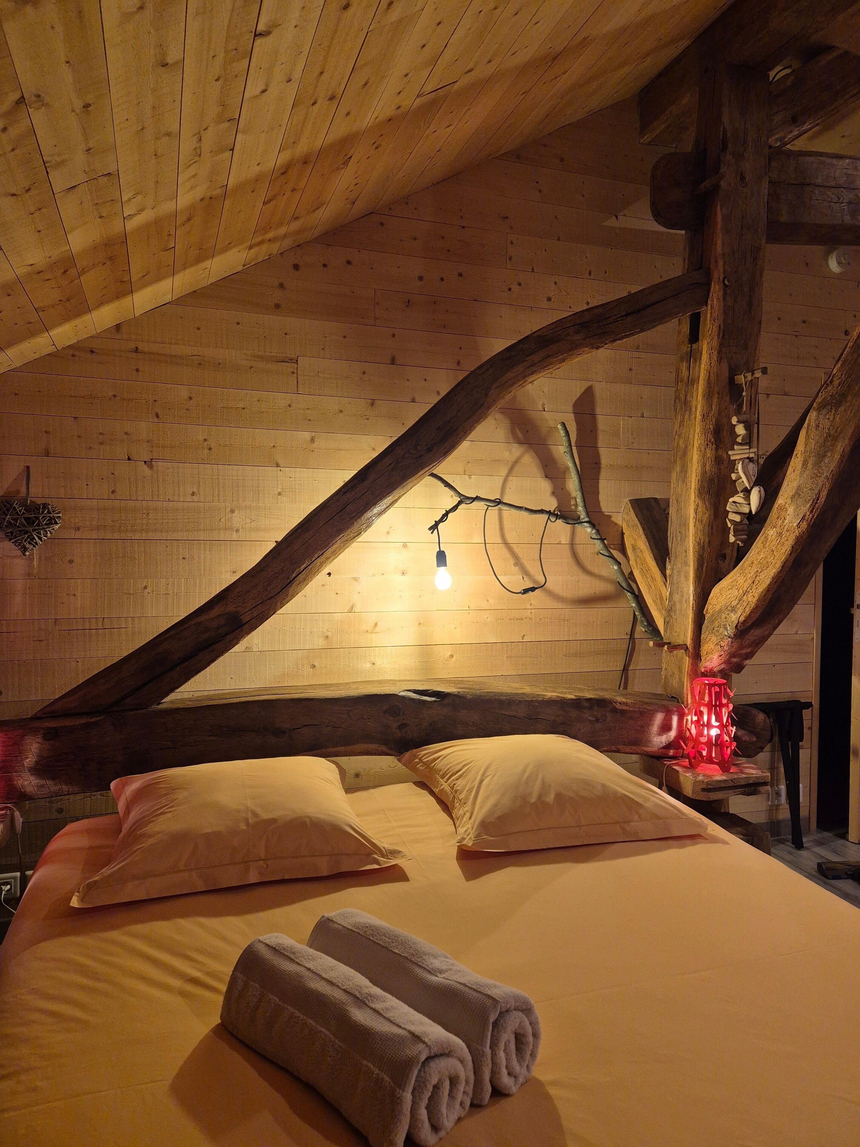 A wooden ceiling with exposed beams, a bed with pillows and rolled towels, and a string of lights.