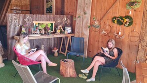 Un interior rústico con paredes de madera, una pequeña mesa con adornos y dos personas sentadas en sillas leyendo libros.