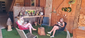 A rustic interior with wooden walls, a small table with decorative items, and two people seated on chairs reading books.