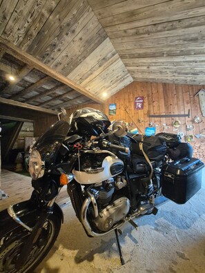 A motorcycle parked inside a wooden-paneled garage with a concrete floor. - “Agathis” Guest Room with Shared Terrace, Garden, and Non-Private Jacuzzi (Vellerot-lès-Vercel)