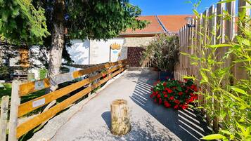 Un chemin menant à un bâtiment entouré d’une clôture en bois, avec un poteau en bois et des fleurs rouges.