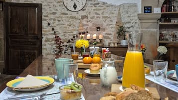 A rustic dining area with stone walls, a wooden table set with breakfast items, and a clock on the wall.