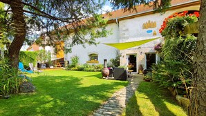 A well-maintained garden with a stone pathway, outdoor seating, and a rustic building with a white facade.