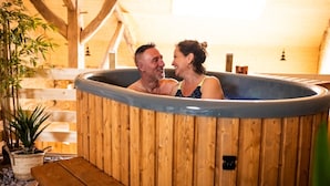 A wooden hot tub with two people inside, surrounded by wooden beams and a staircase. - Guest Room “La Cabane et Spa Chez Jules” with Private Space and Wi-Fi (Vellerot-lès-Vercel)