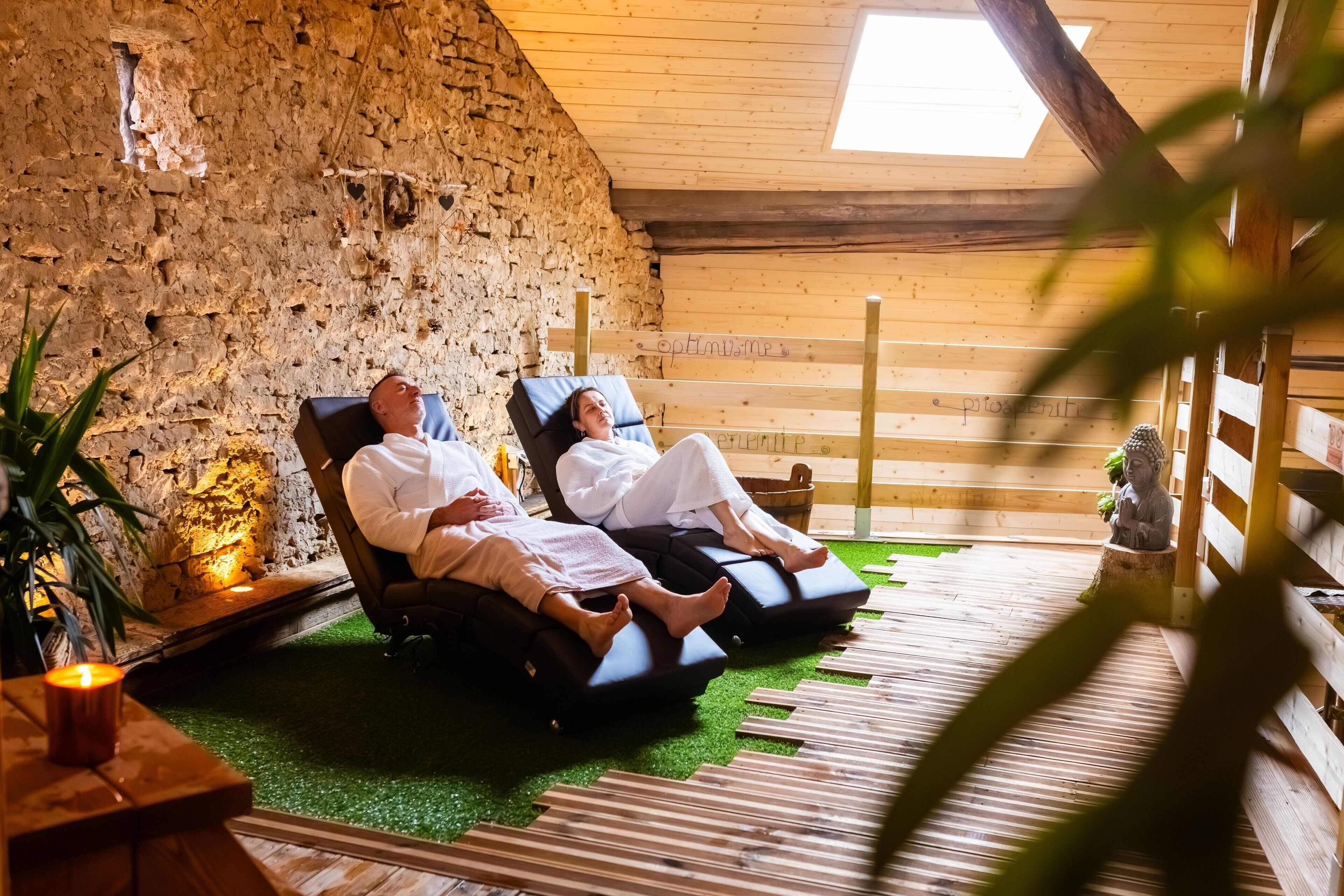 Deux personnes se détendent sur des fauteuils de massage dans une pièce dont les murs sont en pierre et le plafond en bois.