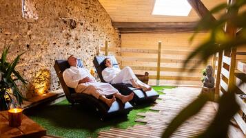 Deux personnes se détendent sur des fauteuils de massage dans une pièce dont les murs sont en pierre et le plafond en bois.
