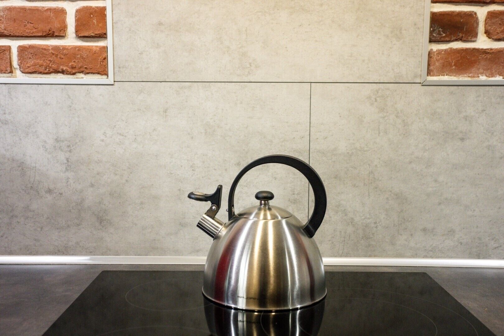 A stainless steel kettle on a black countertop with a tiled wall behind it.