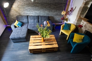 Un salon moderne avec un canapé d’angle, une table basse en bois agrémentée d’un arrangement floral, et deux fauteuils avec des coussins.