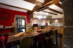 A modern kitchen with exposed brick walls, wooden beams, and a large wooden table with colorful chairs. - Gîte Chez Jules with Spa, Private Terrace, and Wi-Fi (Vellerot-lès-Vercel)