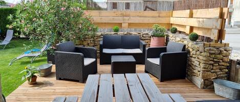 An outdoor patio with wicker furniture, a stone wall, and a wooden deck.
