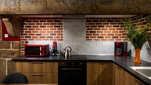 A kitchen with a brick wall, a red microwave, a kettle, and a coffee maker. - Gîte Chez Jules with Spa, Private Terrace, and Wi-Fi (Vellerot-lès-Vercel)