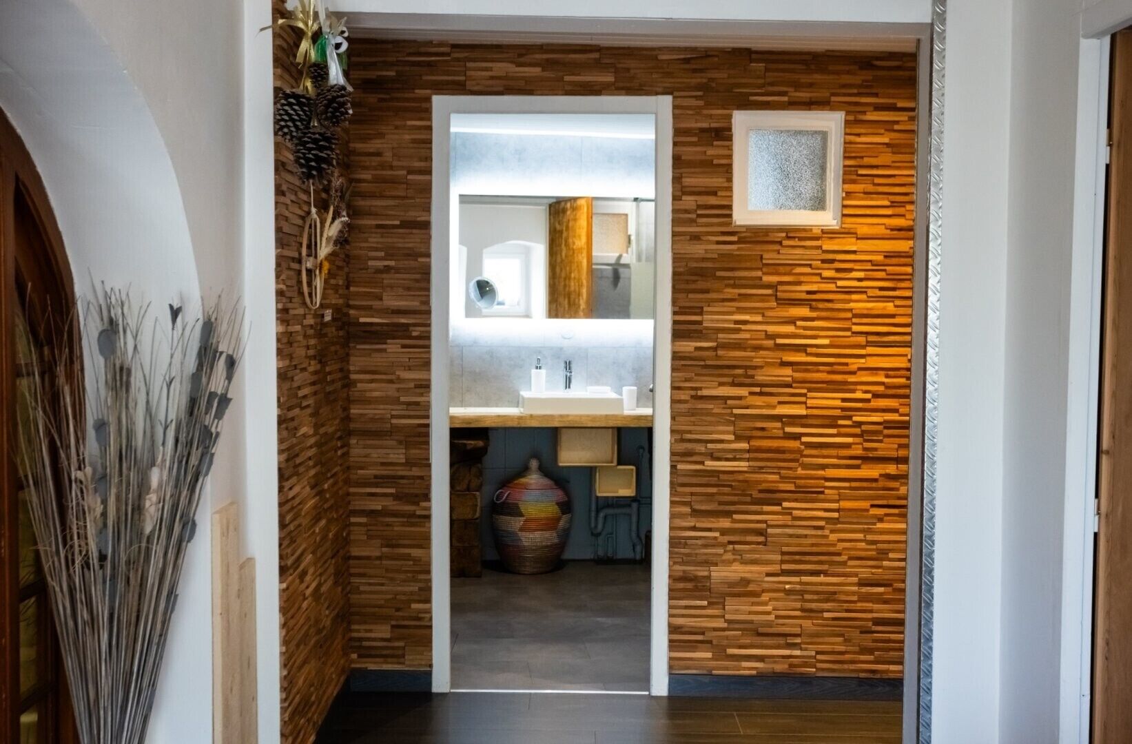 A hallway with a wooden wall and a mirror above a sink.