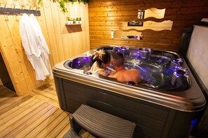 A wooden room with a hot tub, towels, and a shelf with plants.