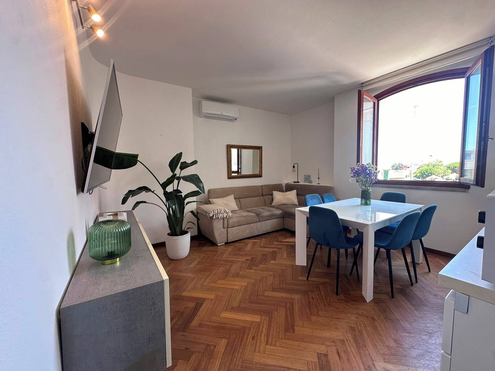 Un soggiorno moderno con un divano, un tavolo da pranzo con sedie, una pianta in vaso e un'ampia finestra.