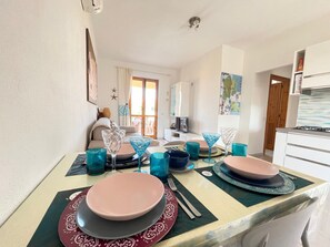 Ein Essbereich mit einem für zwei Personen gedeckten Tisch, einer Couch im Hintergrund und einer angrenzenden Küche rechts.