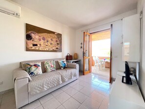 A living room with a beige sofa, colorful cushions, a painting on the wall, and a view to an outdoor patio area. - Holiday Home 'St5 Sunset House Puntocasabudoni' with Mountain View, Wi-Fi and Air Conditioning (San Teodoro)