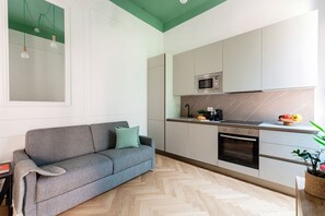 Eine moderne Küche mit grauem Sofa, Mikrowelle, Backofen und einem Fischgrätparkett.