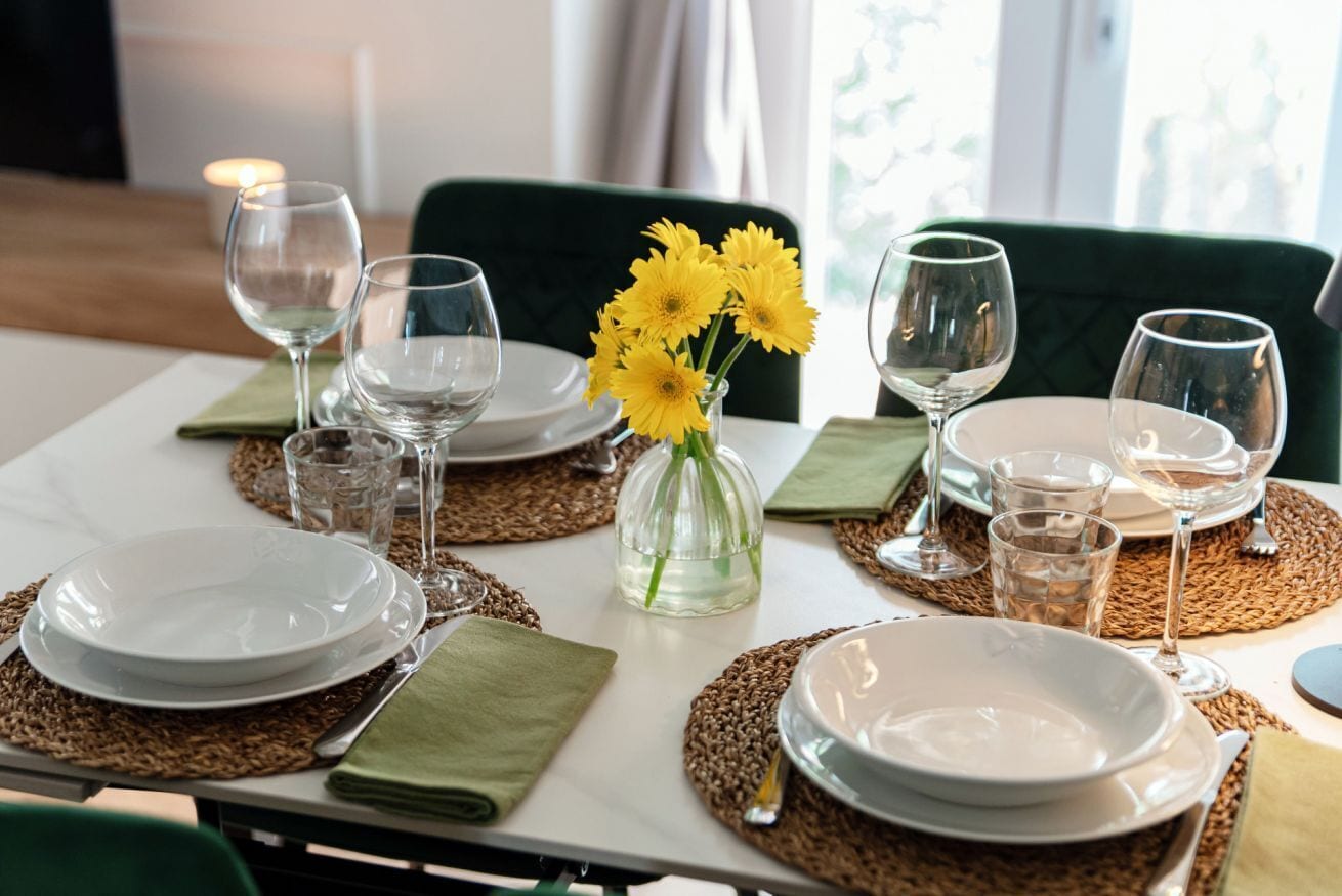 A table set with plates, glasses, and a vase of yellow flowers.