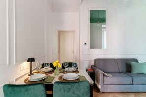 A dining area with a table set for four, a sofa, and a door leading to another room. - Incanto 107 - My Home in Como (Como)