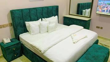 A hotel room with a large bed, a bedside table with a phone, a dresser, a mirror, and a television on the wall.