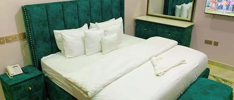 A hotel room with a large bed, a bedside table with a phone, a dresser, a mirror, and a television on the wall.