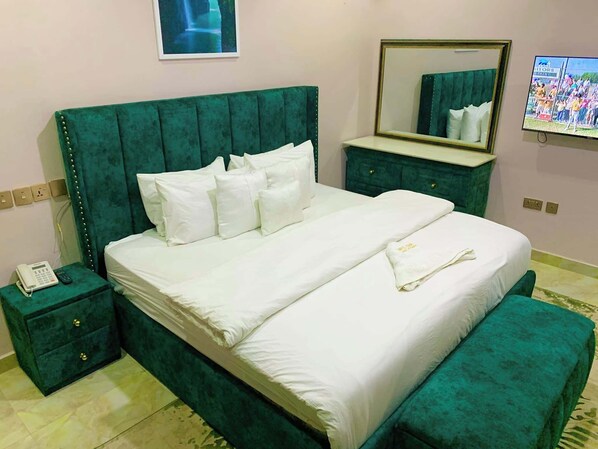 A hotel room with a large bed, a bedside table with a phone, a dresser, a mirror, and a television on the wall.