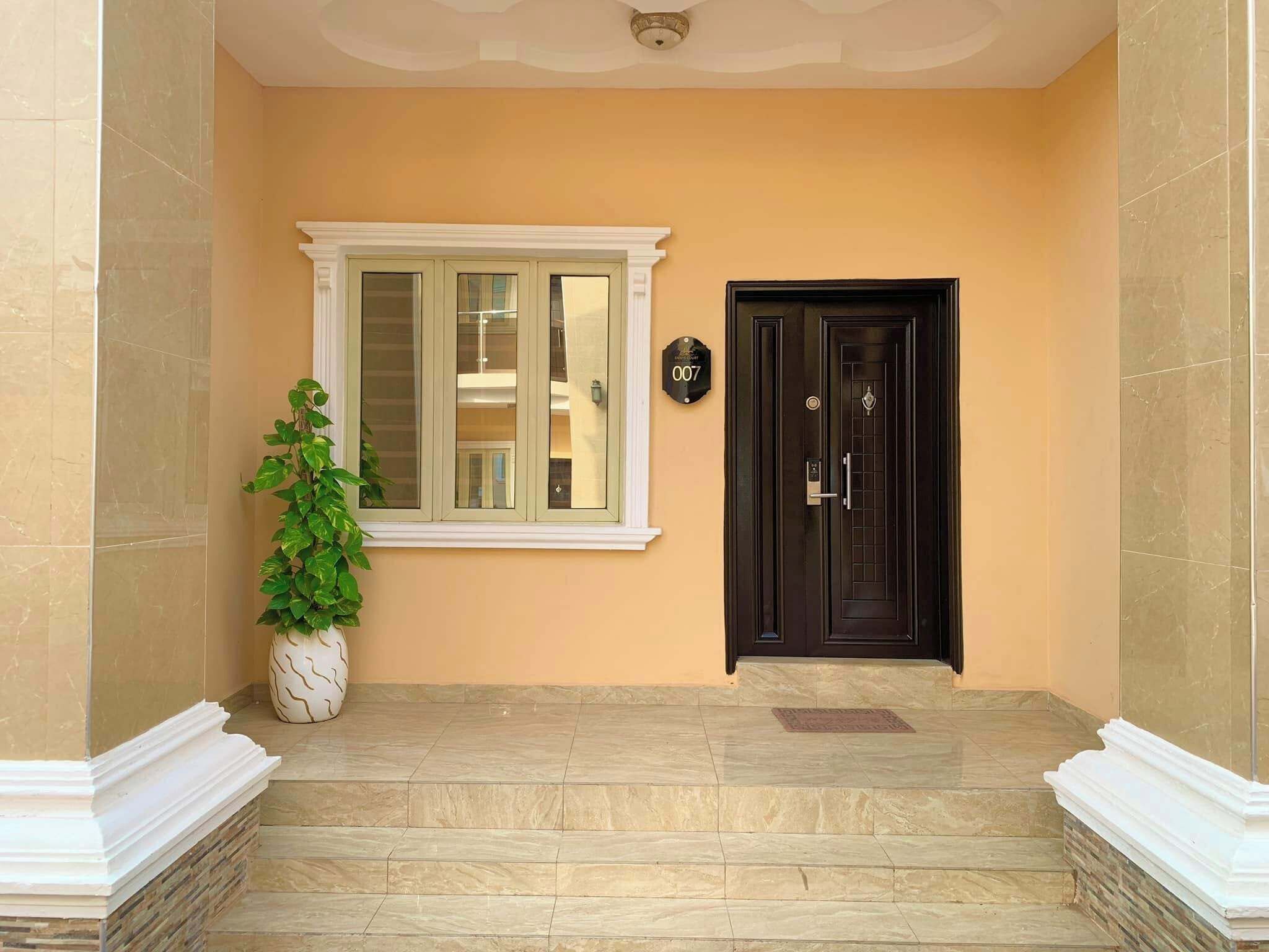 A building entrance with a black door, a window with a white frame, and a potted plant.
