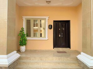 A building entrance with a black door, a window with a white frame, and a potted plant.