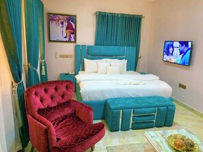 A bedroom with a bed, a red chair, a TV, and a nightstand.