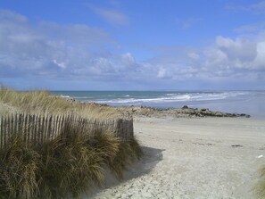 A sandy beach with a wooden fence, a rocky outcrop, and the ocean in the background.