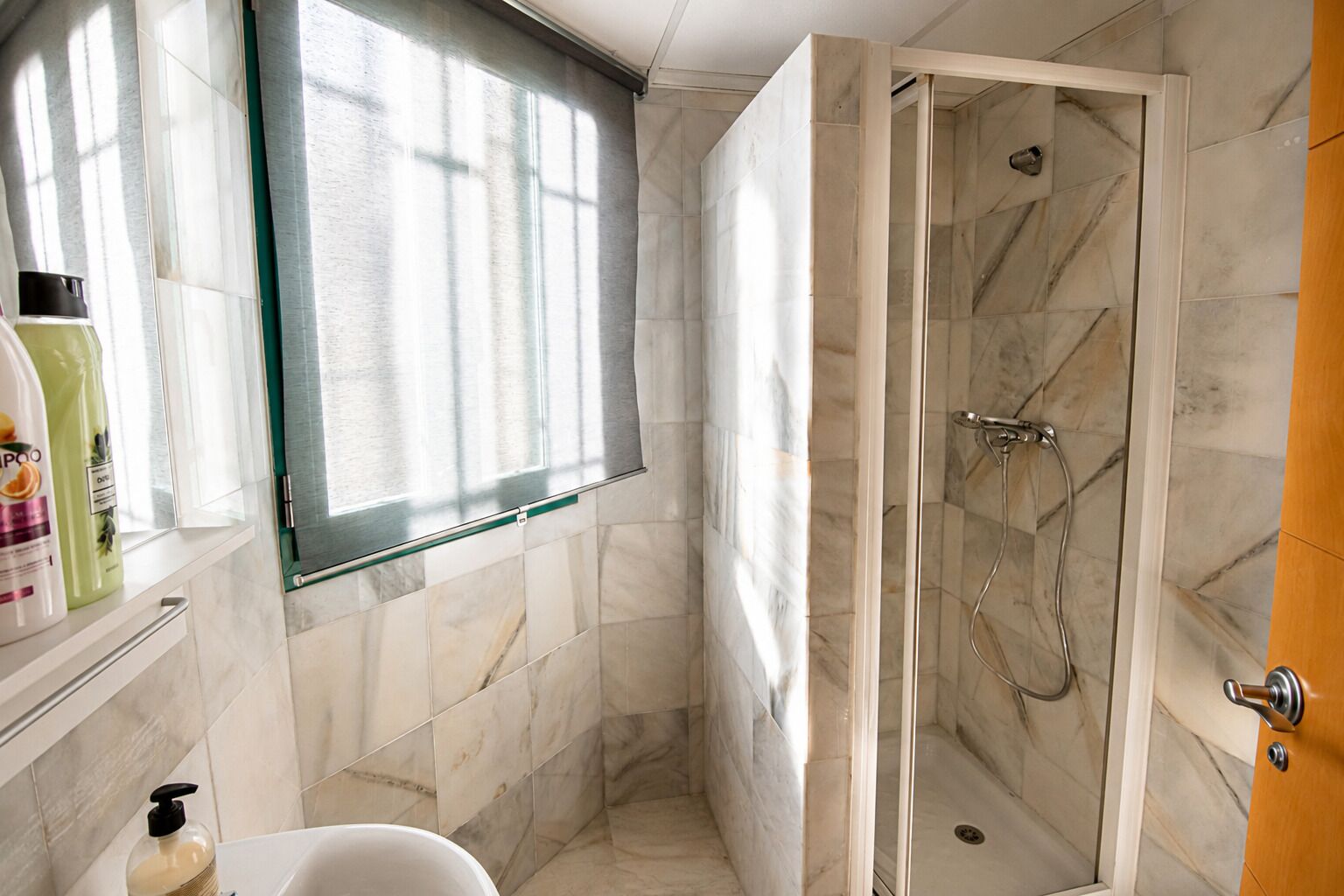Een badkamer met een douche, een raam en toiletartikelen op de counter.