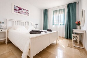 Un dormitorio moderno con cama, mesitas de noche, escritorio, espejo y ventana con cortinas.